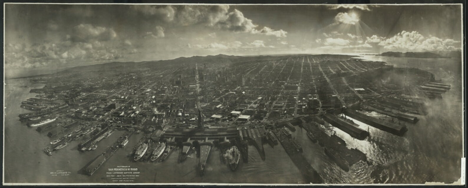 Panoramic aerial photograph of San Francisco in ruins after the April 1906 earthquake and fire, taken from a kite-borne camera 2,000 feet above San Francisco Bay by photographer George R. Lawrence in May 1906. The image shows the waterfront pier system extending into the Bay and the burned interior of the city.